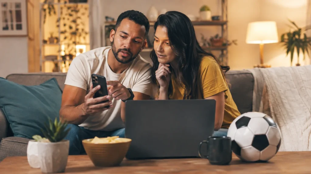 Couple comparing football live-streaming options on phone and laptop